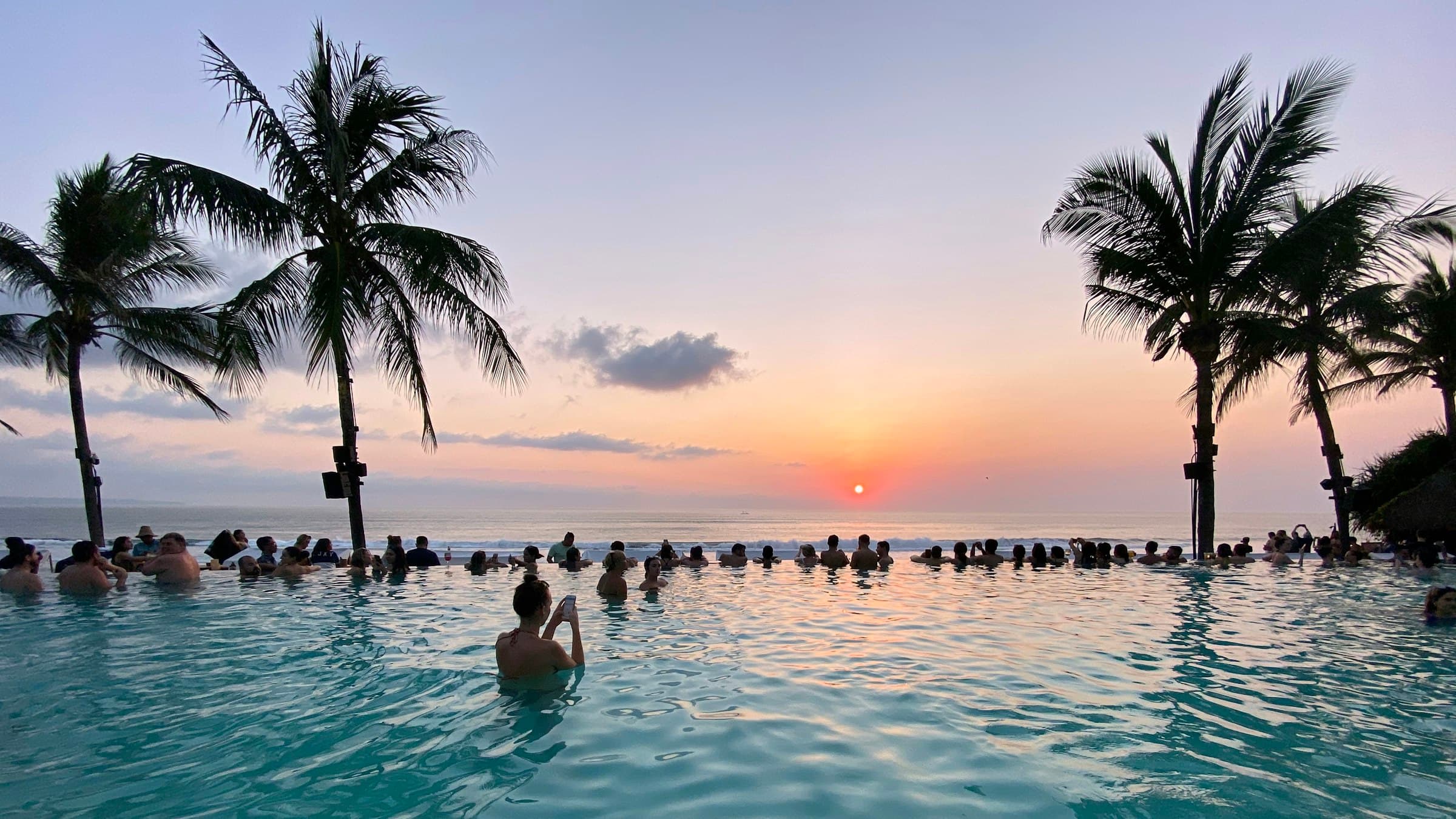 W Bali pool deck at golden hour, coconut palms framing the ocean horizon.